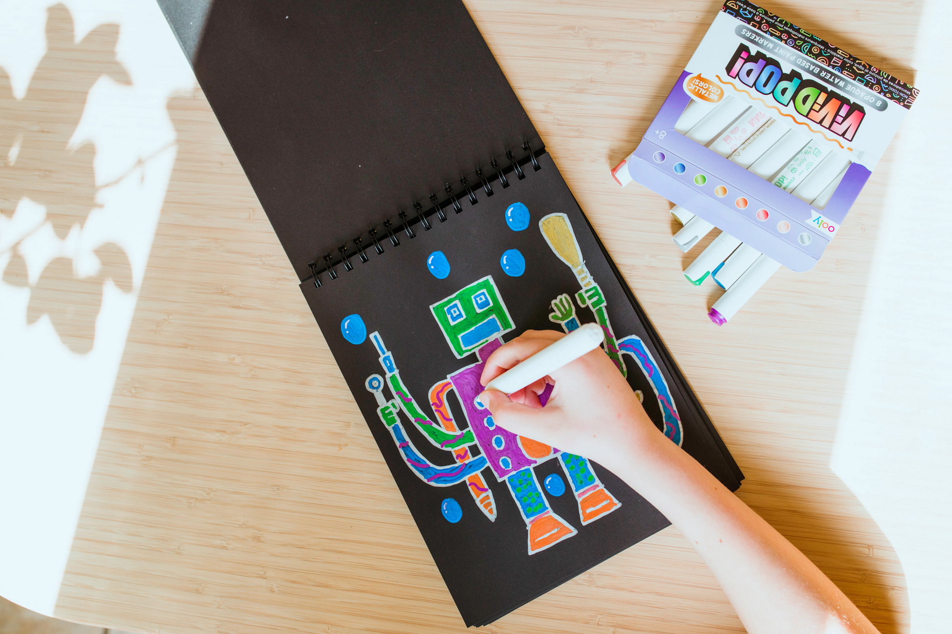 Kid coloring drawing of robot on black paper with OOLY Vivid Pop! Metallic Paint Markers