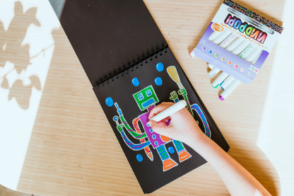 Kid coloring drawing of robot on black paper with OOLY Vivid Pop! Metallic Paint Markers