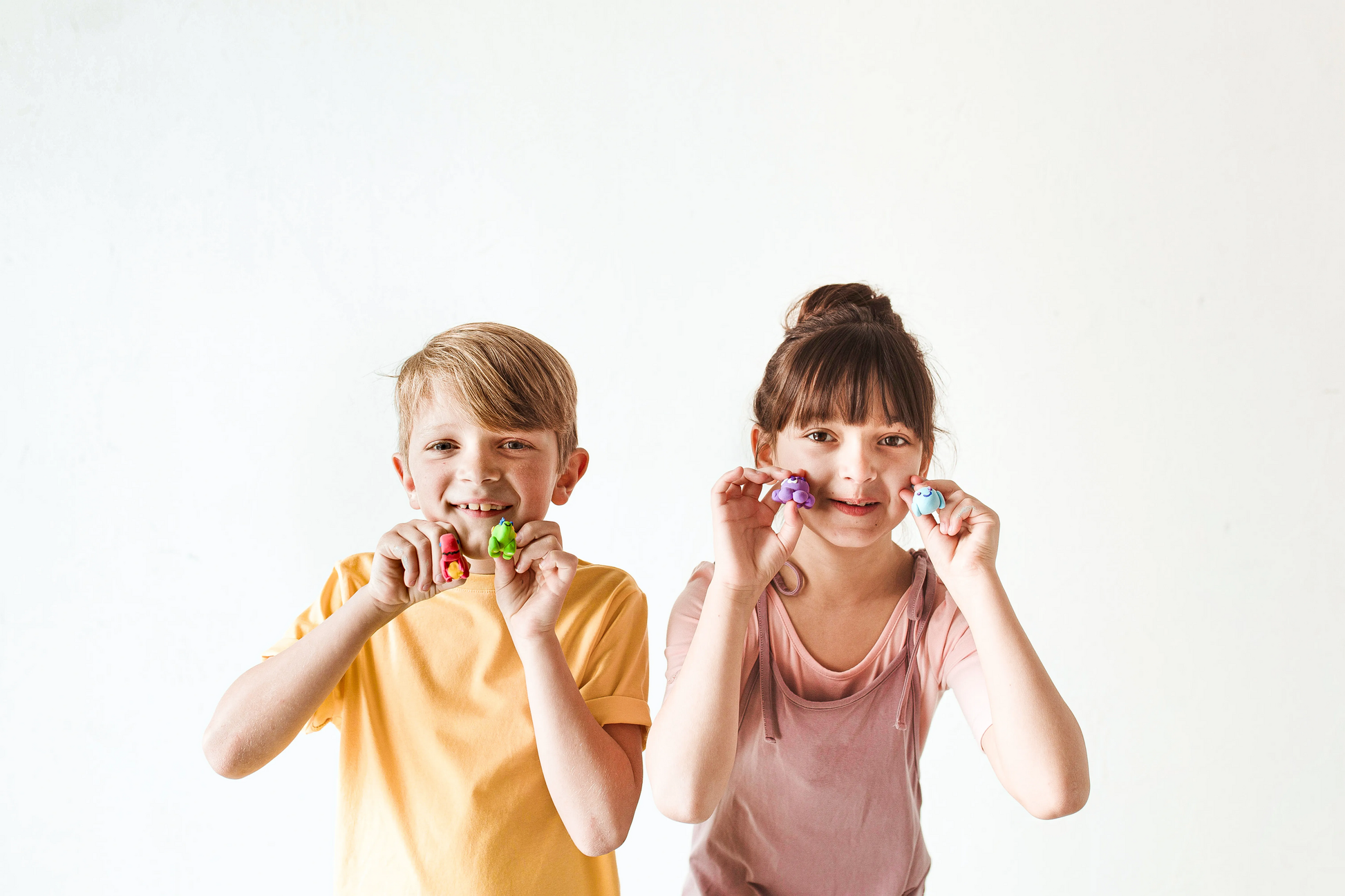 Boy and girl holding completed clay animals from OOLY Creatibles Mini Air Dry Clay Kits