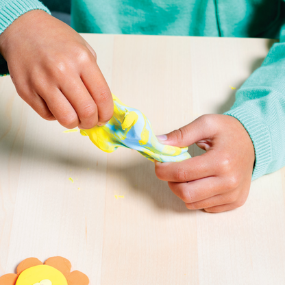 Kid combining blue and yellow clay from OOLY Creatibles Deluxe Air Dry Clay Kit