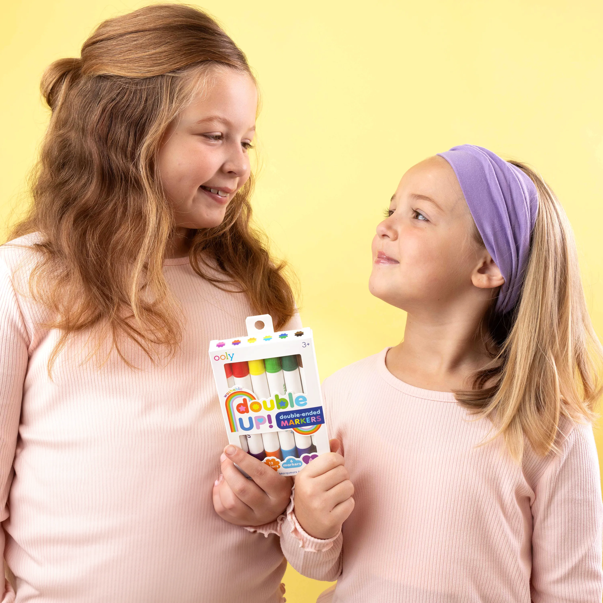 Two girls holding a set of Double Up! Double-Ended Markers with yellow background