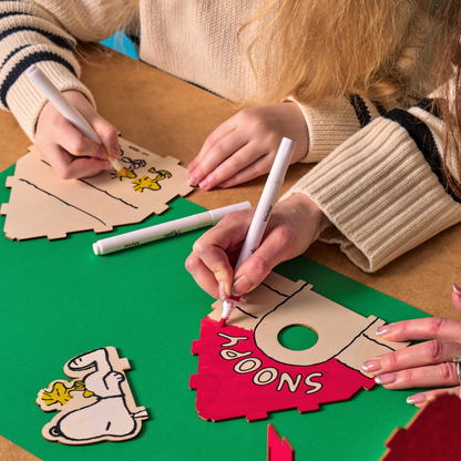 Closeup of two people coloring front of Snoopy birdhouse from the OOLY x Peanuts Color-in Wooden Birdhouse Kit