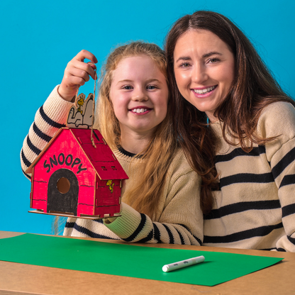 Woman and girl holding a completed birdhouse from the OOLY x Peanuts Color-in Wooden Birdhouse Kit
