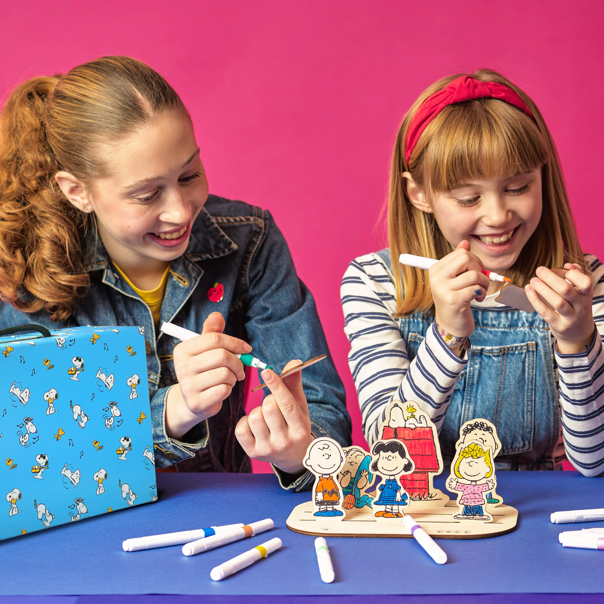 Two people coloring wood pieces with markers from the OOLY x Peanuts Color-In Wooden Scene Kit