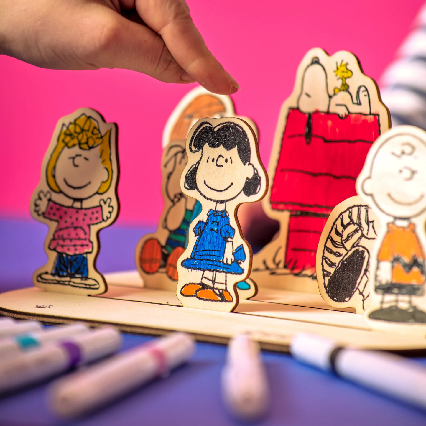 Person placing colored wooden piece of Lucy with other Peanuts characters from the OOLY x Peanuts Color-In Wooden Scene Kit