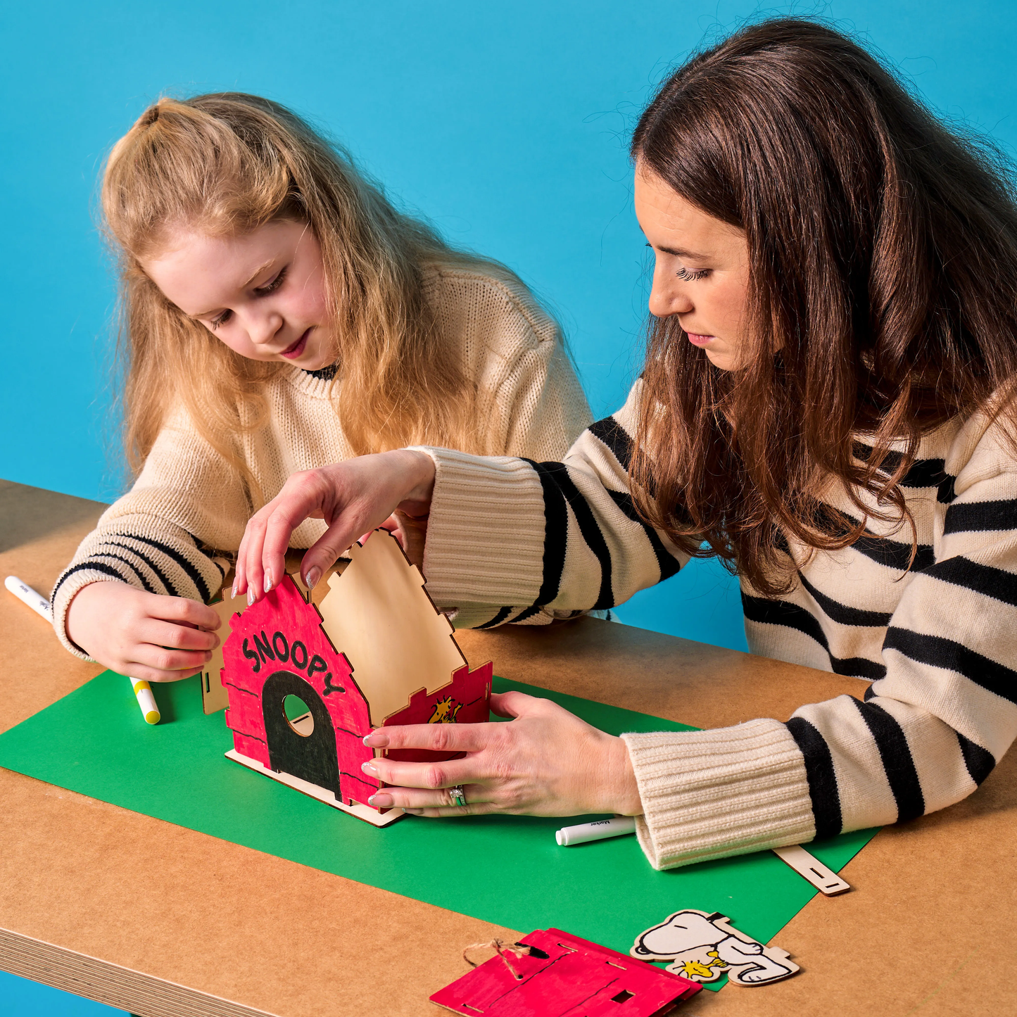 Woman and girl building an OOLY x Peanuts Color-in Wooden Birdhouse Kit