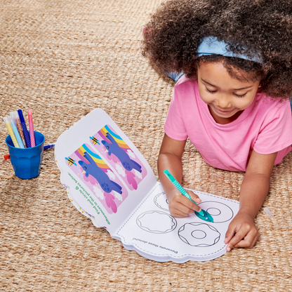 Girl on floor coloring donut in OOLY Playful Pages Activity Book - Games Coloring Stickers - Unicorn Party!