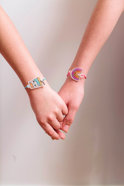 Two hands holding with finished milk shake and rainbow charm bracelets from OOLY Shrink-its! DIY Shrink Art Bracelet Kit - BFF