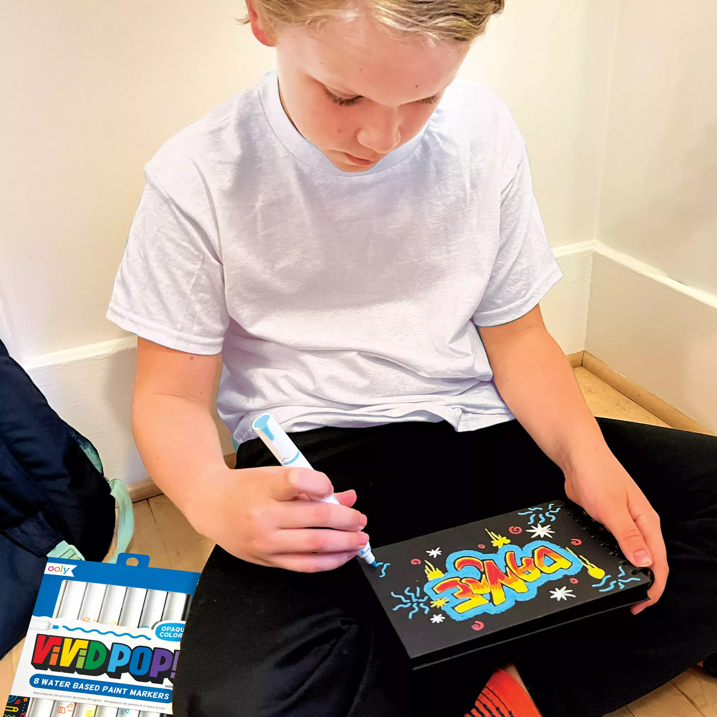 Kid coloring on black paper pad with OOLY Vivid Pop! Water Based Paint Markers