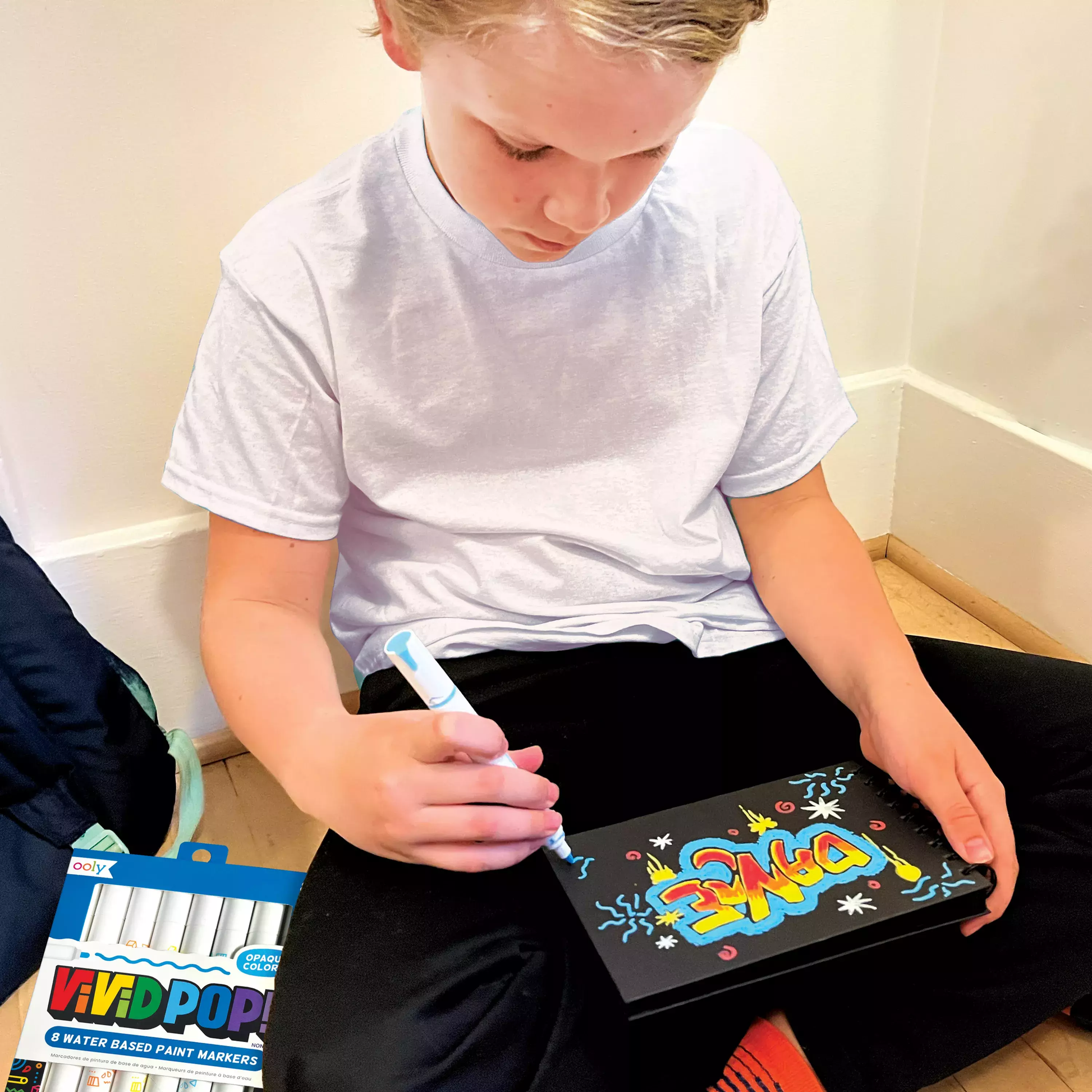 Kid coloring on black paper pad with OOLY Vivid Pop! Water Based Paint Markers