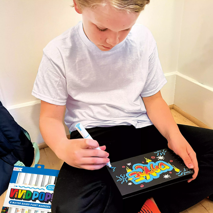 Kid coloring on black paper pad with OOLY Vivid Pop! Water Based Paint Markers